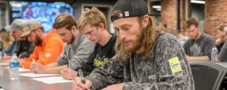 A group of young men sit at a table, focused on writing on papers in a classroom setting.
